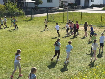 Schulkinder joggen über einen Rasen