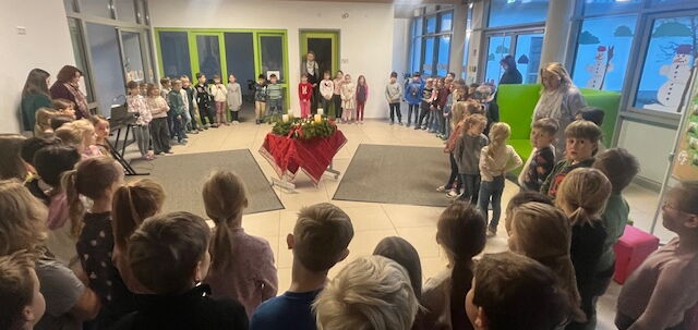 Die Schulfamilie steht im Kreis um den Adventskranz in der Aula