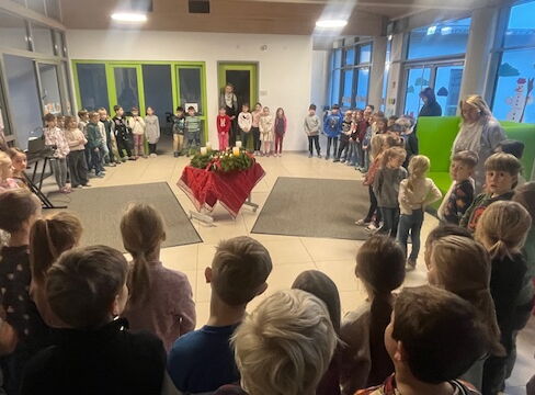 Die Schulfamilie steht im Kreis um den Adventskranz in der Aula