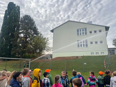 Die Feuerwehr spritzt mit einem Wasserschlauch in Richtung Schulgebäude