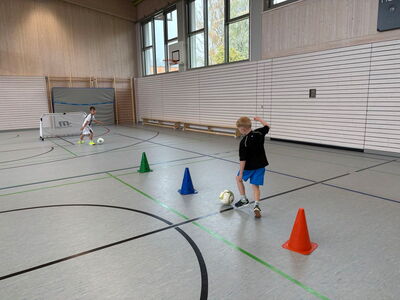 Ein Schüler spielt einen Ball im Slalom in Richtung eines Tores