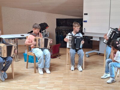 Schüler sitzen im Kreis auf Stühlen und spielen Töne auf Harmonikas und Akkordeons