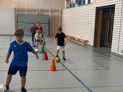 Ein Schüler spielt einen Ball im Slalom in Richtung eines Tores