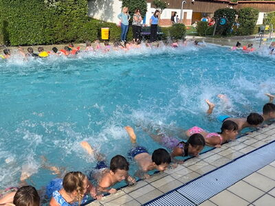 Grundschüler führen entlang des Beckenrandes Beinübungen durch